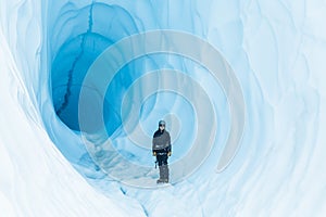 Woman in black standing in a large ice cave of blue ice in Alaska