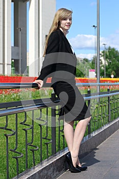 Woman in black suit poses near railing in sunny town