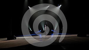 A woman in black suits goes on stage to a microphone in the dark.