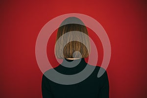 Woman in black sweater and with hairstyle bob isolated on red background, standing with her back to the camera. Back of a girl photo