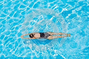 Woman with black swimsuit swimming on a blue water pool