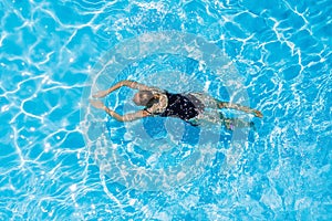 Woman with black swimsuit swimming on a blue water pool