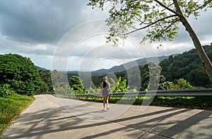 Woman in black t-shirt enjoying tropical forest view while standing on a empty road. Mountains and white clouds on a