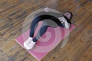 A woman in a black t-shirt performs a fitness exercise on stretching the muscles of the back. Healthy lifestyle. Parquet floor in