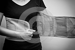 Woman in black t-shirt wearing back support belt for back pain and spinal support. Black and white tone. Medical care concept