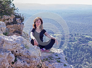 Woman in a black tracksuit sitting on the cliff