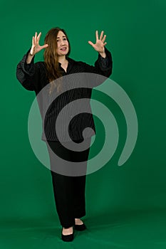 woman in a black trouser suit gesticulates with her hands with her fingers spread out on green background shows talking