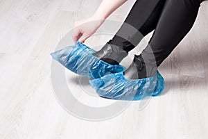 a woman in black trousers sits and takes off her shoe covers, black leather boots, light wooden floor,