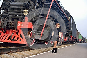A woman in a black vintage dress against the old locomotive