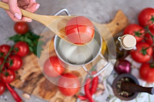 woman blanching a tomato holding over pan with hot water for further peeling