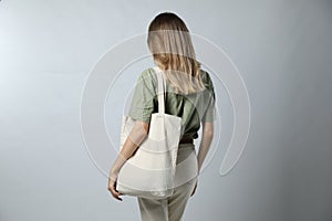 Woman with blank eco friendly bag on light background, back view