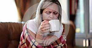 A woman in a blanket on the couch drinks tea, close-up