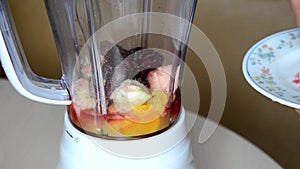 Woman blending strawberry banana, ice to make a healthy red smoothie. Woman pouring a green detox juice from blender to