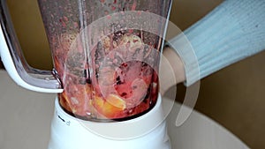 Woman blending strawberry banana, ice to make a healthy red smoothie. Woman pouring a green detox juice from blender to