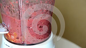 Woman blending strawberry banana, ice to make a healthy red smoothie. Woman pouring a green detox juice from blender to