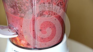 Woman blending strawberry banana, ice to make a healthy red smoothie. Woman pouring a green detox juice from blender to