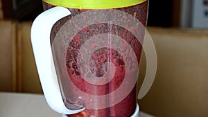 Woman blending strawberry banana, ice to make a healthy red smoothie. Woman pouring a green detox juice from blender to