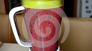 Woman blending strawberry banana, ice to make a healthy red smoothie. Woman pouring a green detox juice from blender to