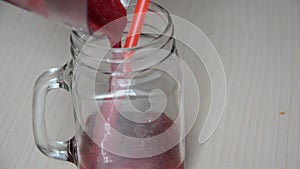 Woman blending strawberry banana, ice to make a healthy red smoothie. Woman pouring a green detox juice from blender to