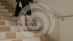 Woman with blindness disability walking down stairs using blind walking stick or long cane and touching stair handrail