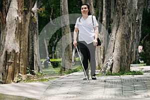 Woman with blindness disability walking on sidewalk contain tactile paving guide blocks using long white cane or blind cane a