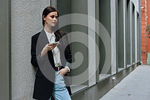 Woman blogger smile with teeth with a phone in her hands walks around the city fashion on the street, spring travel