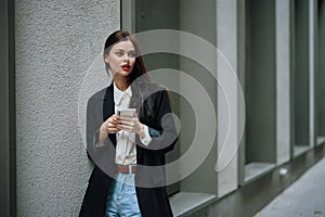 Woman blogger smile with teeth with a phone in her hands walks around the city fashion on the street, spring travel