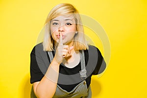 Woman with blond dyed hair putting her finger on her lips in a studio