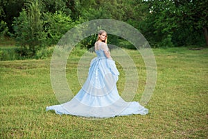 Woman with blond hair in a beautiful blue dress with a long sleeves outdoor on the lawn or in the forest. Romantic art photo