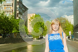 Woman blonde in blue dress walking along a city street against a background of urban architecture and summer Siberian beauties