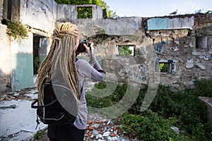 Woman with blonde dreadlocks takes pictures of Abandoned buildings.