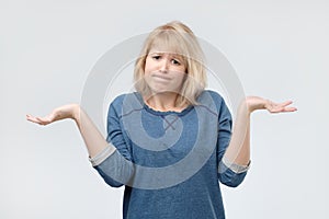 Woman with blonde hair looking in confusion, shrugs shoulders as do not know answer, being clueless