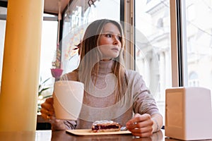Woman with blonde hair sips cappuccino in a cafe. She is holding the glass up to her face, taking a sip of the drink.