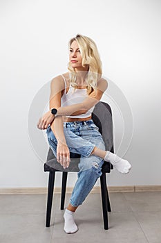 Woman with blonde hair sitting on chair. Lovely millennial lady posing, relaxing indoors