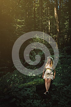 Woman with blonde hair sitting on a tree in the forest. Beautiful fairy tale light in fantasay landscape