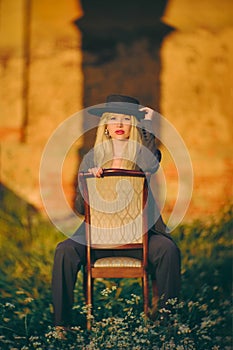 Woman blonde in a hat. Portrait. Lady sitting on a chair in nature. Abstract background.