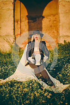 Woman blonde in hat sitting on chair in nature on background of old building with arches. Lady is holding an aquarium