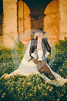 Woman blonde in hat sitting on chair in nature on background of old building with arches. Lady is holding an aquarium