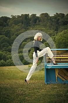 Woman in blonde wig playing piano in retro style interior with leg in shoe