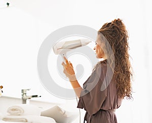 Woman blow drying hair in bathroom