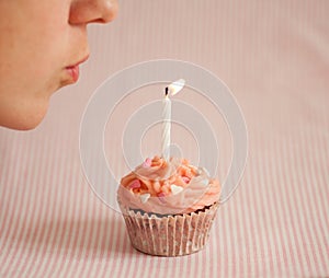 Woman blowing a candle on a pink cupcake