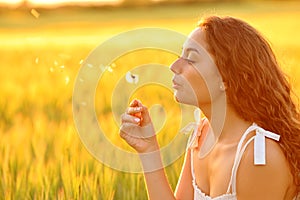 Woman blowing a dandelion in a wheat field at sunset
