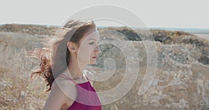 Woman with blowing hair in dress looks far and raises head to sky among cliffs