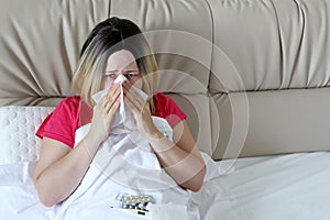 Woman blowing her nose in a handkerchief sitting in a bed