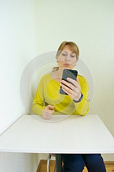 Woman blowing a kiss in smartphone communicates in online chat and social networks with her close people sitting at home on white