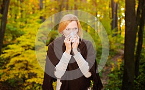 Woman blowing nose with handkerchief In autumn park. Seasonal virus infection. Chronic disease.