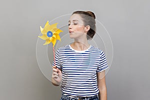 Woman blowing at paper windmill, playing with pinwheel toy on stick.