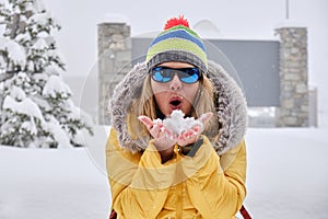 Woman blowing snow from her hands, wearing colorful yellow clothes in Winter.