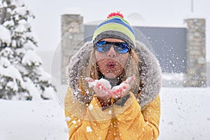 Woman blowing snow from her hands, wearing colorful yellow clothes in Winter.