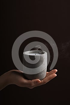 Woman with blown out candle in concrete holder against dark brown background, closeup